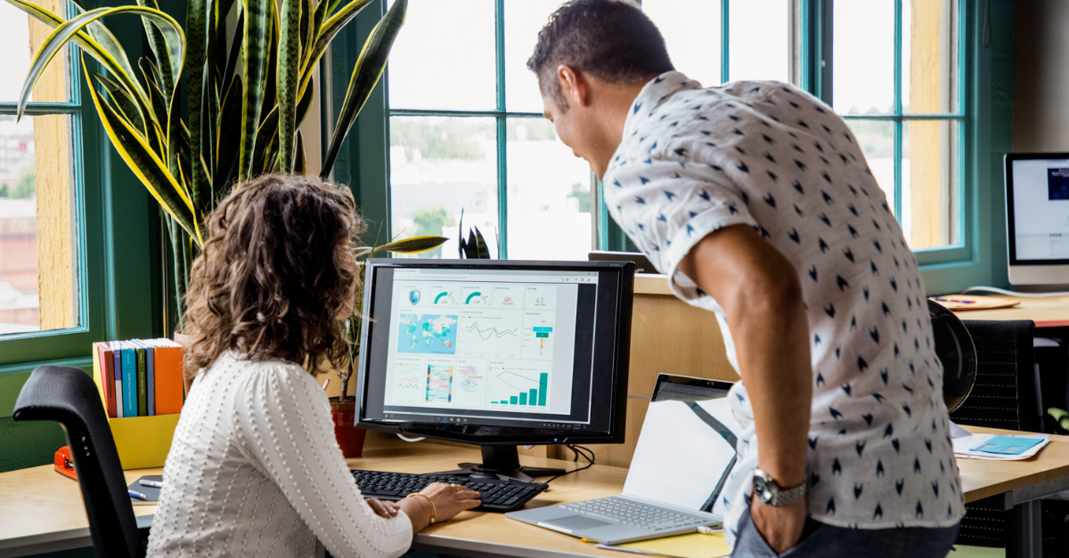 A woman showing her male coworker charts on her computer screen.