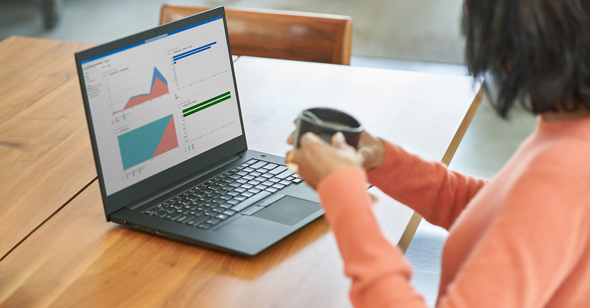 A woman looking at her laptop, holding a cup