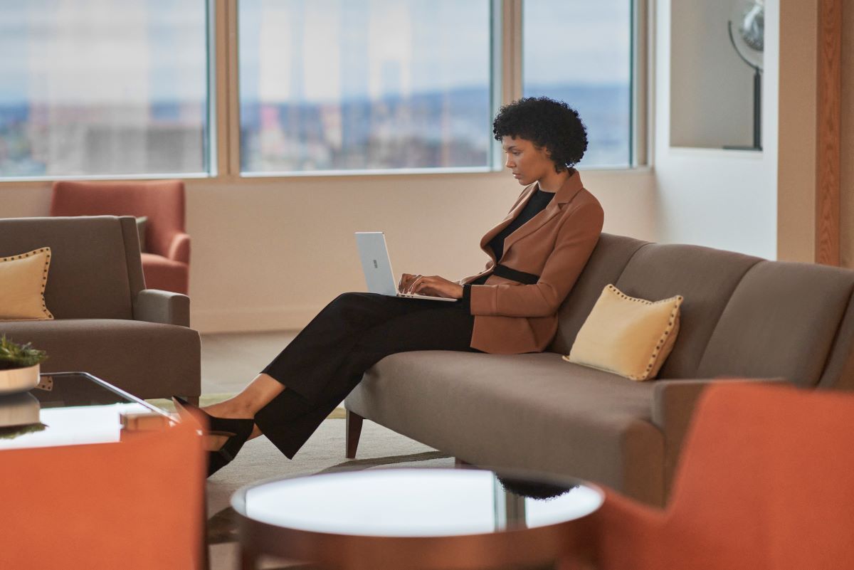 A woman on a sofa in a casual office using a laptop.