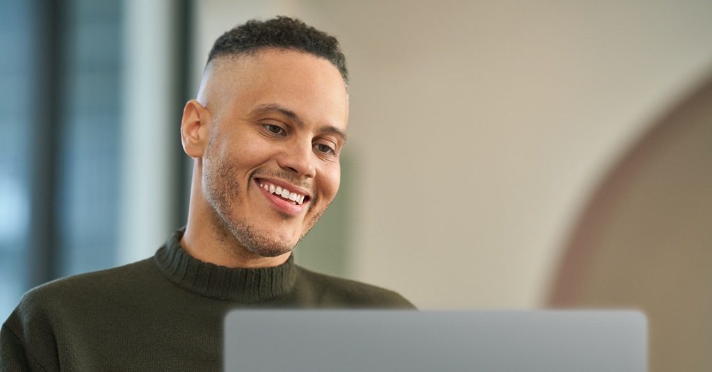 A smiling young man using a laptop.