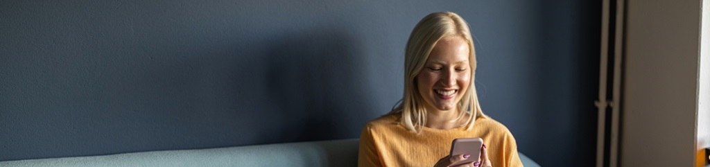 A young woman looking at her phone and smiling.