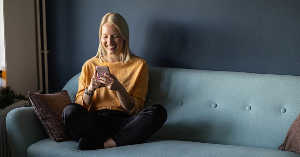 A young woman looking at her phone and smiling.