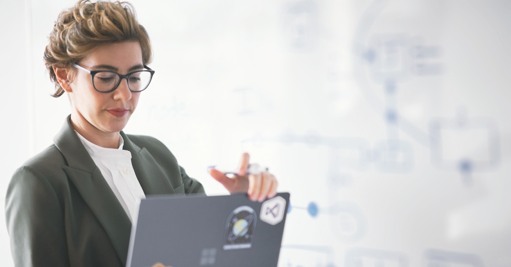 A young professional woman holding a laptop in front of a whiteboard.