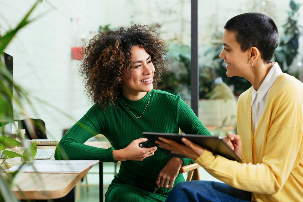 a person in a green shirt, talking with a person in a yellow shirt and holding a digital tablet together.