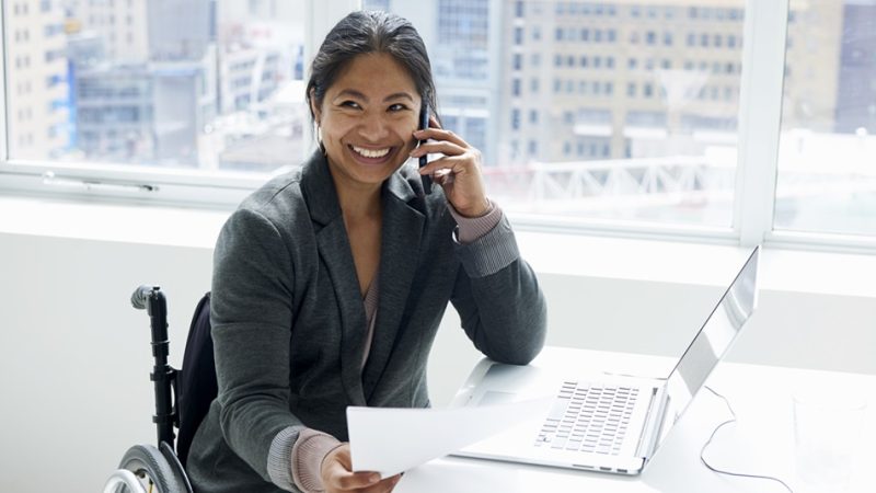 Mujer sonriente en silla de ruedas trabajando en una oficina.