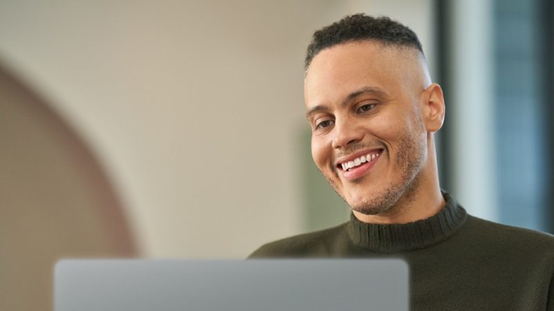 Un joven sonriente usando una computadora portátil.