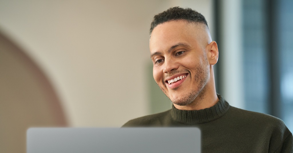 Un joven sonriente usando una computadora portátil.