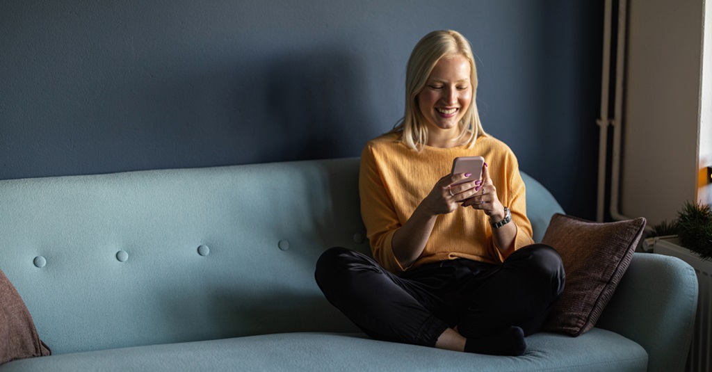 Una mujer joven mirando su teléfono y sonriendo.