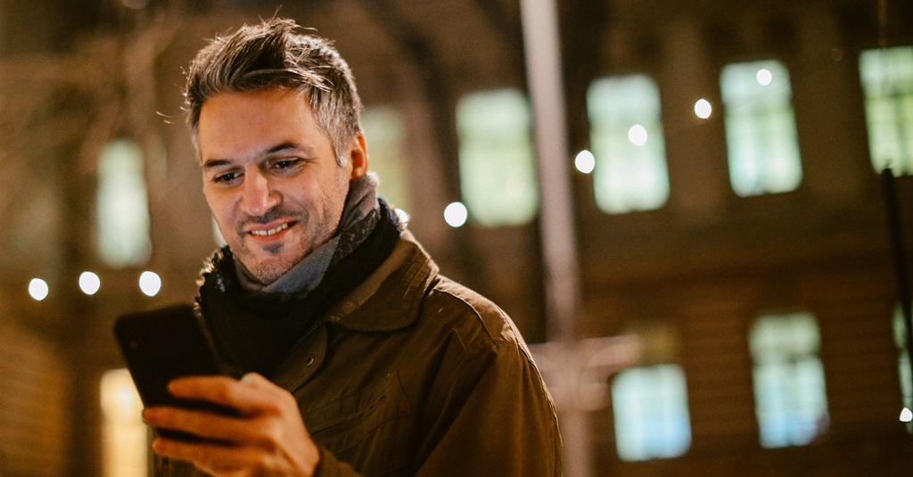 Un homme dehors par une nuit froide regardant son téléphone.